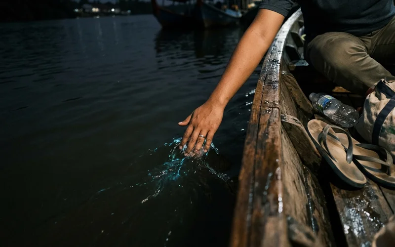 A hand trailing in dark river water showing a subtle glow where the water is disturbed