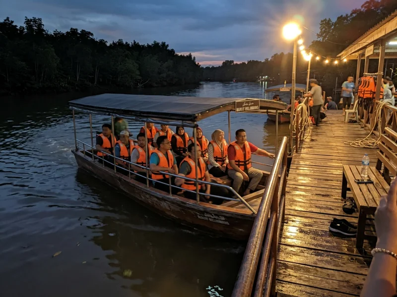 A covered electric boat leaving the lit jetty at Bukit Belimbing in the evening
