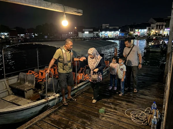 A covered electric boat at a lit river jetty in the evening