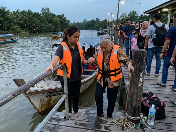 A guide helping an older traveller board a river boat at the jetty